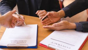 Close-up of three pairs of hands over two agreement contracts on an office table in Singapore