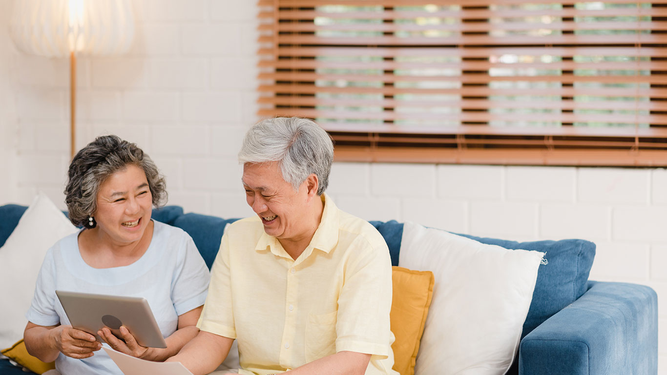 A retired couple with grey hair on a sofa look at a tablet in Singapore