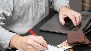 Wallet, cash and coins on a table as man works on a laptop in Singapore